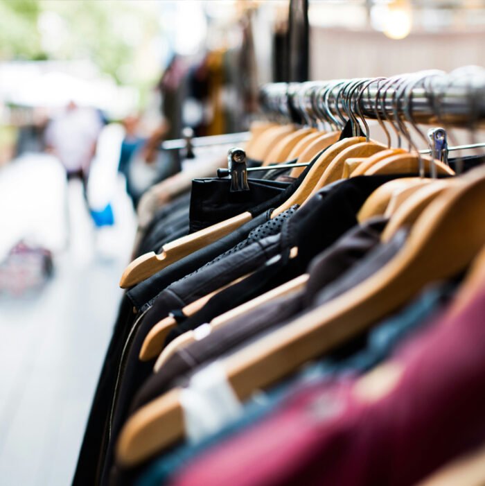 Clothes on hangers at a store with people in the background.