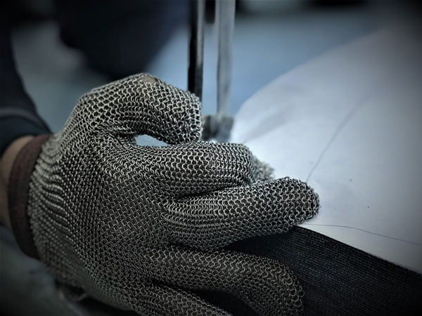 Craftsperson in a Turkish clothing manufacturing company expertly cutting fabric, adorned with a protective metal mesh glove.