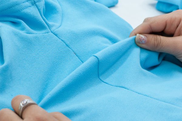Hands inspecting the texture of a blue fabric for top-tier clothing production.