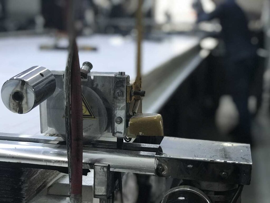 Clothing manufacturing factory with cutting machine, skilled worker, and background workers inspecting garments.